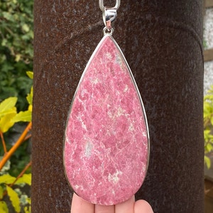 May include: A teardrop-shaped pendant made of pink rhodochrosite gemstone set in sterling silver.