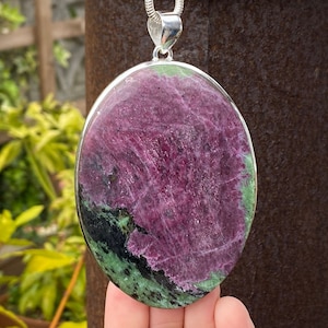 May include: Oval-shaped pendant featuring a green and pink gemstone with silver bail. The gemstone has a swirling pattern of green, pink, and black.