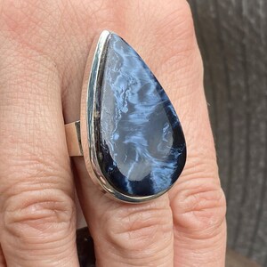 May include: A large, teardrop-shaped ring featuring a polished blue and white gemstone set in a silver band. The stone has a swirling pattern, and the ring is displayed on a finger.