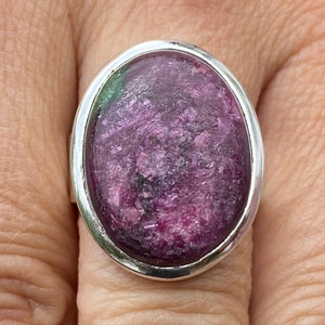 Pode incluir: Um anel de prata com uma grande gema oval rosa e verde engastada em uma moldura de prata.