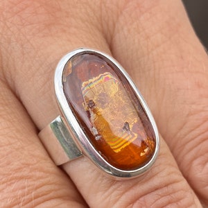 May include: A silver ring with an oval-shaped amber stone. The stone has a unique iridescent pattern and is set in a silver bezel.