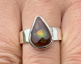 May include: A teardrop-shaped ring with a brown, green, and gold agate stone set in a silver band.
