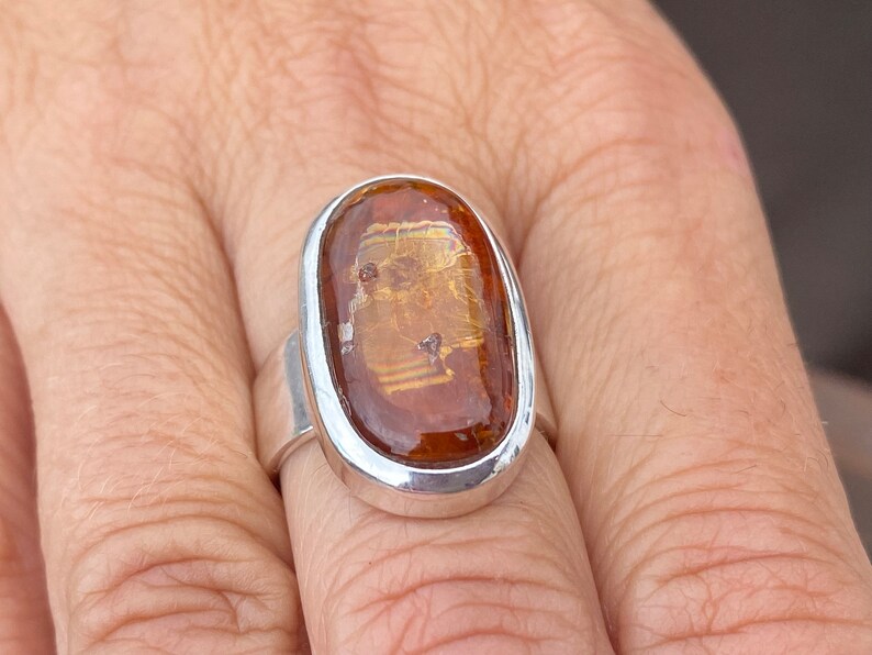 May include: A silver ring with a large oval-shaped amber stone set in a bezel setting. The stone has a golden hue and is translucent.