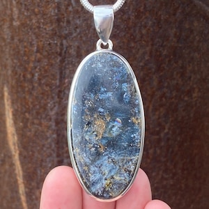 May include: A silver oval pendant featuring a blue and gold iridescent stone. The stone has a swirling pattern and a shimmering finish.