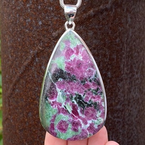 May include: A teardrop-shaped pendant featuring a green, pink and white gemstone set in sterling silver. The gemstone has a distinctive pattern of swirls and inclusions.