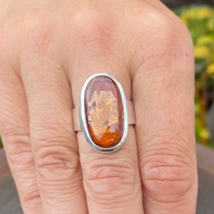 May include: A silver ring with an oval-shaped amber stone. The stone has a warm, honey-like color and is set in a simple, elegant band.