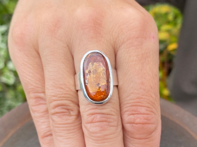 May include: A silver ring with an oval-shaped amber stone. The stone has a warm, honey-like color and is set in a simple, elegant band.