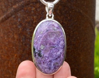 May include: A silver pendant featuring a large oval-shaped purple and black stone with a swirling pattern. The stone is set in a silver bezel.