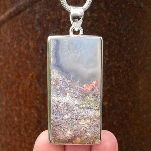 May include: A silver pendant featuring a rectangular, clear stone with a layered pattern of white, grey, and brown. The stone has a natural, organic look.