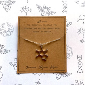 May include: A brown card with the text "Glucose, The essential molecule for respiration and the body's main source of energy."  A silver necklace with a glucose molecule pendant hangs from the card. The text "Personal Message Here" is printed on the bottom of the card.