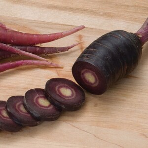 May include: A whole purple carrot and several slices of the carrot on a wooden cutting board. The carrot has a dark purple exterior and a light purple interior with a white core.