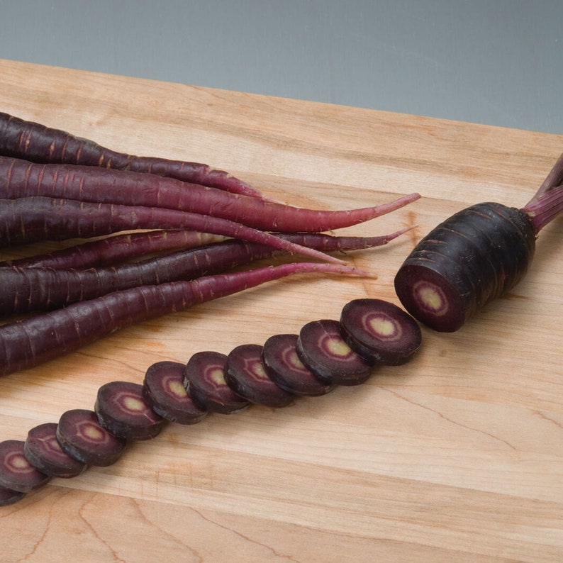 May include: Purple carrots on a wooden cutting board. The carrots are sliced and whole. The slices reveal a white core.
