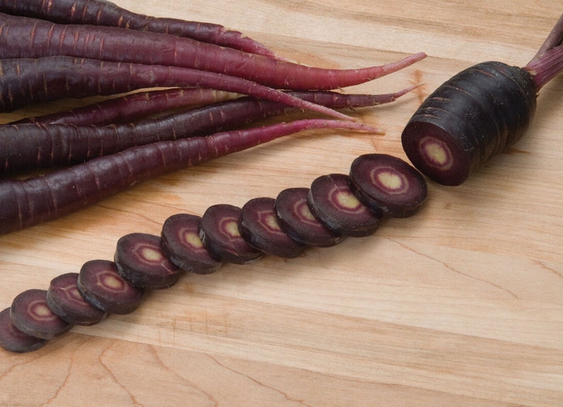 May include: Purple carrots sliced on a wooden cutting board. The carrots are arranged in a line with the cut ends facing the viewer. The carrots are a deep purple color with a white core.