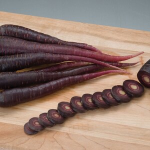 May include: A bunch of purple carrots on a wooden cutting board. Some of the carrots are sliced, revealing a white core.
