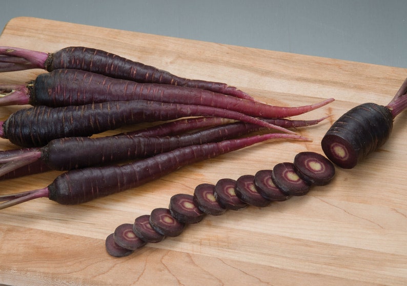 May include: A bunch of purple carrots on a wooden cutting board. Some of the carrots are sliced, revealing a white core.