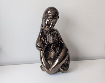May include: A bronze-colored ceramic sculpture of two figures embracing. The figures are stylized and abstract, with smooth, flowing lines.