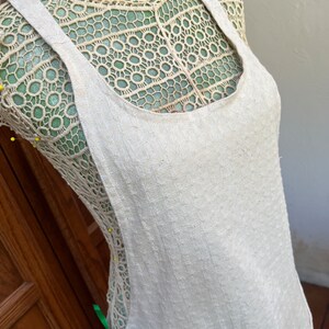 May include: A white linen apron with adjustable straps. The apron is on a dress form with a lace bodice.