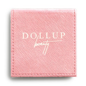 May include: A pink, square-shaped makeup compact with the text "DOLLUP beauty" in white lettering.