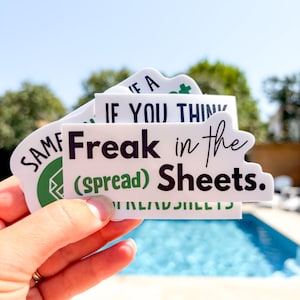May include: A stack of white vinyl stickers with black and green text. The top sticker features the text "Freak in the (spread) Sheets." in a mix of bold sans-serif and cursive fonts. Other visible stickers include text fragments like "IF YOU THIN" and "SAME".