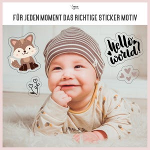 May include: A baby wearing a striped hat and a beige onesie is looking up and smiling. There are three stickers on the image: a fox, a plant, and a sticker that says "hello world!" with hearts.