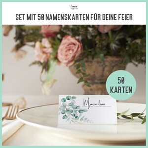 May include: A set of 50 blank place cards with a watercolor design of green leaves and gold accents. The cards are on a white plate with a gold rim. The text "Maximilian" is written on one of the cards. A sign in the background reads "50 Karten".