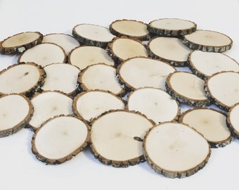 May include: A pile of round, natural wood slices with bark edges. The wood is light brown and the bark is a darker brown. The slices are various sizes and are arranged in a random pattern.