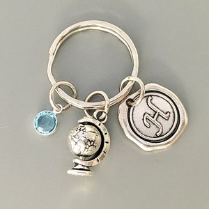Puede incluir: Llavero de plata con un dije de globo terr&aacute;queo, un dije de cristal azul y un dije de plata con la letra "H" en &eacute;l.