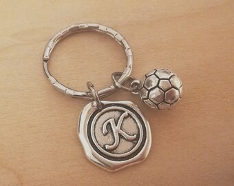 May include: Silver keychain with a soccer ball charm and a silver charm with the letter K.