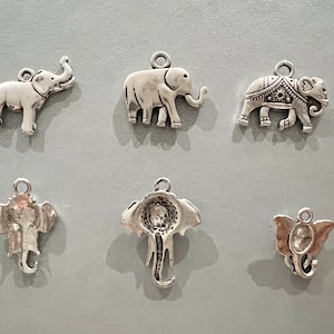 May include: Six silver elephant charms with different designs. The charms are all approximately 5 cm tall and have a loop at the top for attaching to a necklace or bracelet.