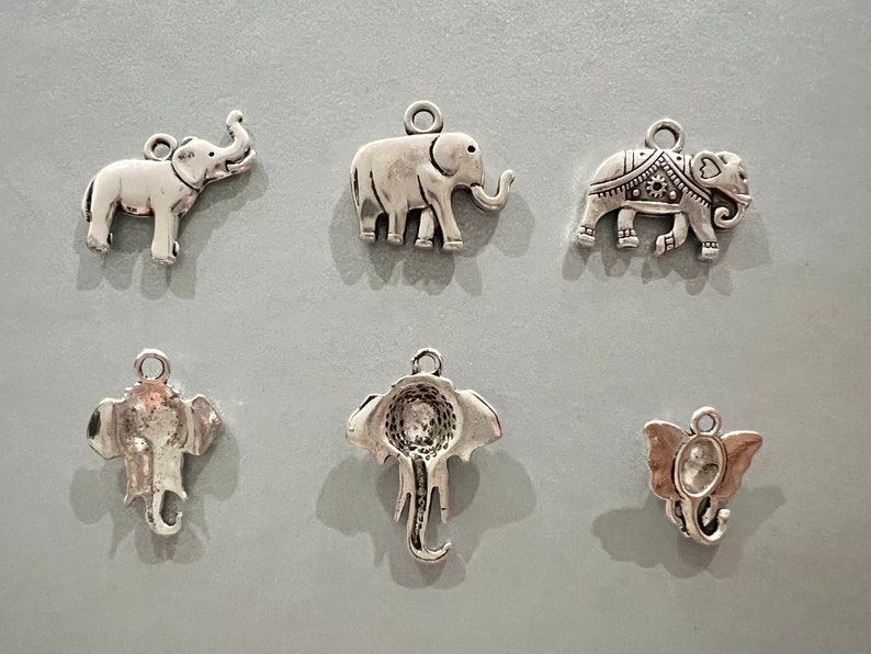 May include: Six silver elephant charms with different designs. The charms are all approximately 5 cm tall and have a loop at the top for attaching to a necklace or bracelet.