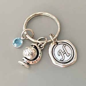Puede incluir: Llavero de plata con un dije de globo terr&aacute;queo, un dije de cristal azul y un dije de plata con la letra H.
