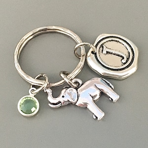 May include: Silver keyring with a green gemstone, a silver elephant charm, and a silver charm with the letter J.