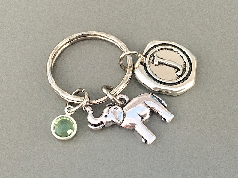 May include: Silver keyring with a green gemstone, a silver elephant charm, and a silver charm with the letter J.