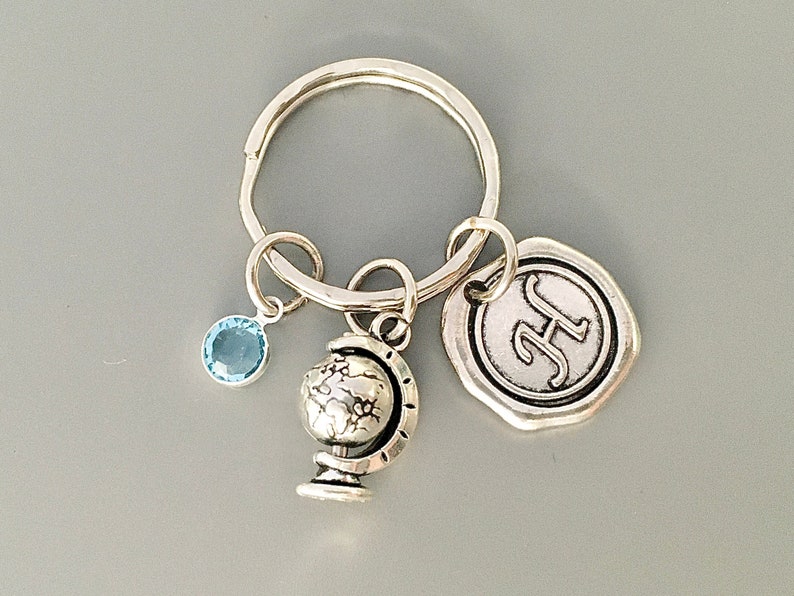 Puede incluir: Llavero de plata con un dije de globo terr&aacute;queo, un dije de cristal azul y un dije de plata con la letra "H" en &eacute;l.