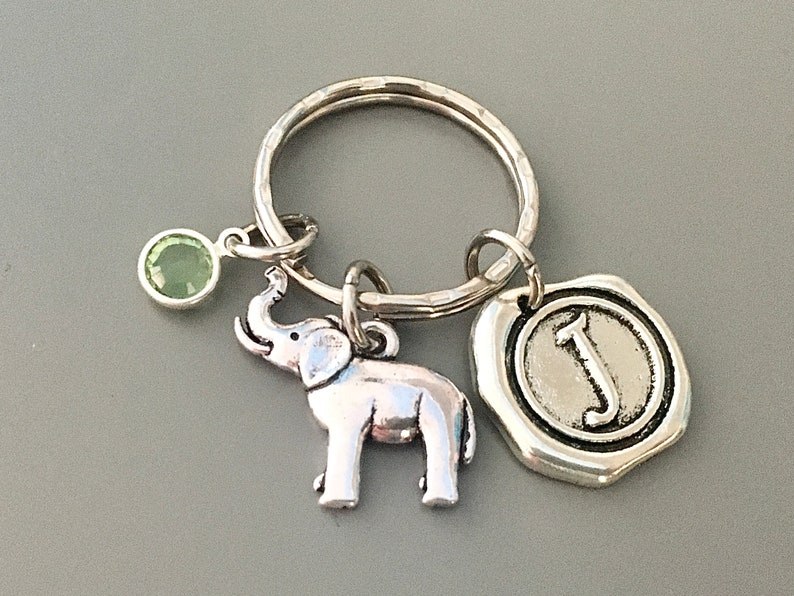 May include: Silver key ring with a green gemstone, a silver elephant charm, and a silver charm with the letter J.