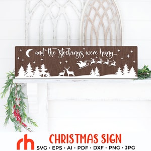 May include: A rectangular wooden Christmas sign with the phrase "and the stockings were hung..." in white script. The sign features a silhouette of a winter scene with trees, deer, Santa's sleigh, and stars. The sign is brown with white accents.
