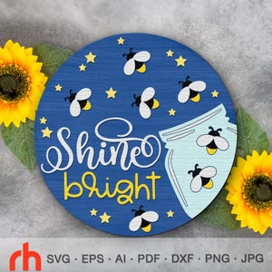 May include: A round, blue wooden sign with the words "Shine bright" in white and yellow. The sign features illustrations of bees, stars, and a jar. Two sunflowers are on either side of the sign.