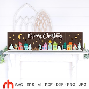 May include: A wooden Christmas sign with the words "Merry Christmas" in white script. The sign features a colorful village scene with houses, trees, and a crescent moon. The background is dark brown.