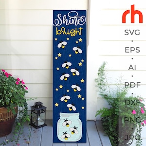 Puede incluir: Un letrero de madera azul marino con las palabras "Shine bright" en blanco y amarillo. El letrero presenta luciérnagas blancas y estrellas amarillas sobre un fondo azul oscuro. Un tarro de cristal con luciérnagas en la parte inferior.