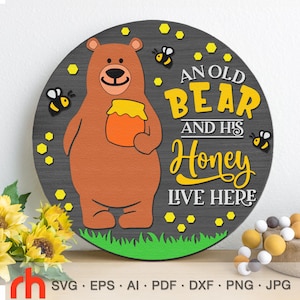 May include: A round wooden sign with a brown bear holding a jar of honey. The sign has the text "An old bear and his honey live here" in yellow letters.