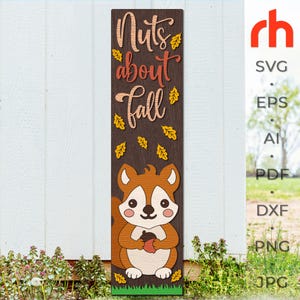 May include: A tall, rectangular wooden sign with a dark brown wood grain finish. The text "Nuts about fall" is written in a script font, accompanied by yellow leaf cutouts. A cartoon squirrel holding an acorn is centered at the bottom.