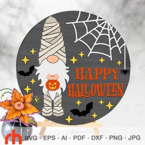 Könnte beinhalten: Ein kreisförmiges Schild mit einem Mumien-Gnom, der einen Kürbis hält, einem weißen Spinnennetz, zwei schwarzen Fledermäusen und gelben Sternen auf dunkelgrauem Grund. Der Text HAPPY HALLOWEEN ist orange. Darunter steht eine Blume in einem grauen Topf.