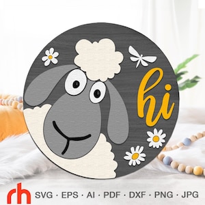 Könnte beinhalten: Ein rundes, graues Holzschild mit einem weißen Schafgesicht und dem Wort "hi" in gelben Buchstaben. Das Schaf hat schwarze Augen und eine weiße Nase. Um das Schaf und das Wort "hi" herum befinden sich weiße Blumen mit gelben Zentren.