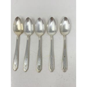 May include: Five silver spoons with oval bowls and ornate, detailed handles. The spoons are arranged in a row, showcasing their polished, reflective surfaces. The handles feature a decorative pattern, adding a touch of elegance to the silverware.