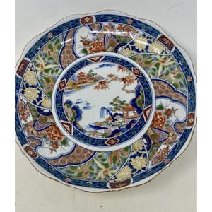 May include: A decorative ceramic plate with a scalloped edge and a gold rim. The plate features a central landscape scene surrounded by floral and geometric patterns in blue, orange, green, and white.