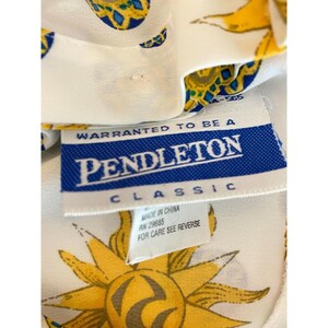 Puede incluir: Primer plano de una tela blanca con un dise&ntilde;o de sol amarillo y azul. Se ve una etiqueta Pendleton Classic azul y blanca, con el texto "Warranted to be a Pendleton Classic".