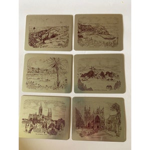 May include: Set of six gold-colored metal coasters with engraved images of landmarks in Exeter, England. Each coaster features a different scene, including the Cathedral, the Quay, and the River Exe.