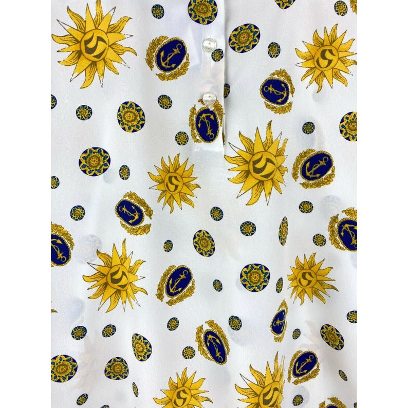 Puede incluir: Camisa blanca con cuello con un patr&oacute;n repetido de soles amarillos, anclas azules y dise&ntilde;os circulares dorados. La camisa tiene una tapeta con botones con tres botones blancos.
