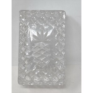 May include: A rectangular clear glass box featuring a faceted diamond pattern across the surface and a central etched pineapple motif on the lid. The glass has a polished finish with geometric detailing along the edges and top.