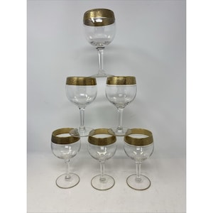 May include: A set of seven clear wine glasses with gold rims. The glasses are arranged in a pyramid shape, with one glass at the top, three in the middle, and three at the bottom. The gold rims add a touch of elegance.